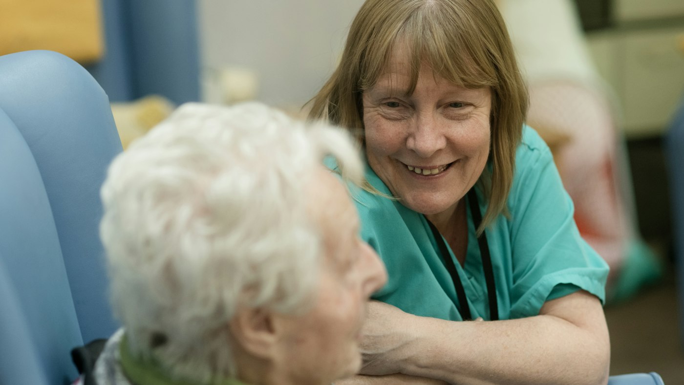 Carer in scrubs talking with an older woman at home