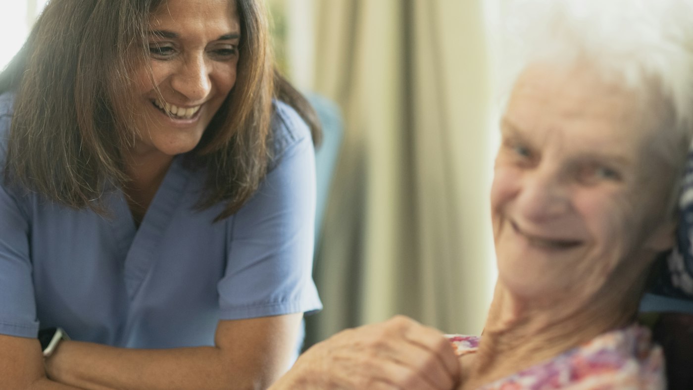 Nurse smiling with an elderly patient in her room